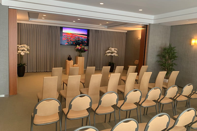 Aula met lichthouten stoelen, grijs gordijn en beeldscherm